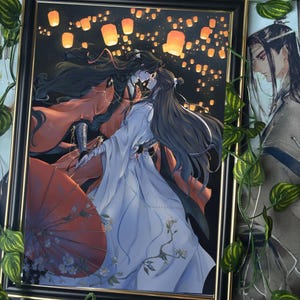 May include: A framed illustration of two people in traditional Chinese clothing standing close together. The man is wearing red and the woman is wearing white. They are surrounded by floating lanterns in the night sky.