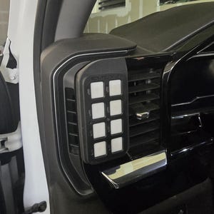 May include: A black control panel with eight white square buttons is mounted on a car's dashboard. The panel is labeled "RGR-TOUCH II". The dashboard is black with silver trim and air vents.