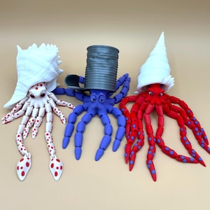 May include: Three colorful octopus figurines with articulated legs, each wearing a different hat. The octopus on the left is white with red polka dots and wears a white seashell. The middle octopus is purple with a gray can on its head. The octopus on the right is red with blue polka dots and wears a white seashell.