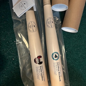 May include: Two wooden baseball bats with personalized names and details. The bats are hand-built and bone-hardened. The bats are 32.5 inches and 33.0 inches long. The bats are packaged in clear plastic bags with brown cardboard tubes.
