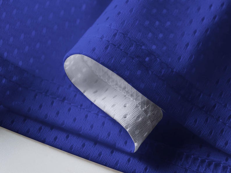 May include: Close-up of a royal blue fabric with a mesh-like texture. The edge of the fabric is folded over, revealing a white interior. The fabric has small, evenly spaced holes, creating a breathable material.
