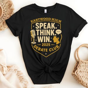 Pode incluir: Camiseta preta com um gráfico dourado que diz "Eastwood High Speak Think Win. 2025 Debate Club". O gráfico apresenta um microfone, um balão de fala e uma cabeça de pessoa.