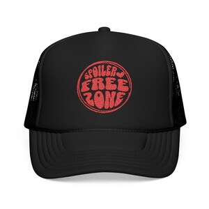 May include: Black trucker hat with a curved brim and mesh back. The front features a red embroidered circular design with the words "SPOILER FREE ZONE" in a retro font. A stylish accessory for casual wear.
