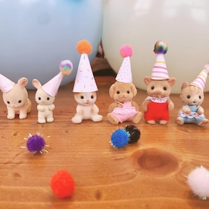 Puede incluir: Un grupo de pequeñas figuras de animales que llevan gorros de fiesta coloridos. Las figuras son de plástico y miden unos 5 cm de alto. También hay varios pompones pequeños esparcidos alrededor de las figuras.