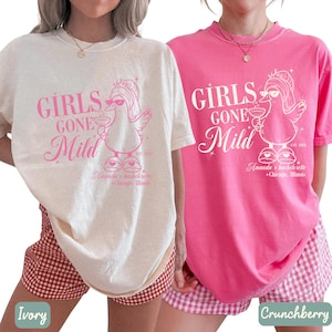 May include: Two t-shirts, one cream and one pink, with the text "GIRLS GONE Mild" and a cartoon duck wearing sunglasses and holding a drink. The text "Amanda's bachelorette + Chicago, Illinois" is also printed on the shirts.
