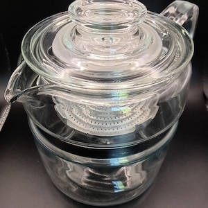 May include: A clear glass coffee pot with a lid and a filter basket. The pot has a spout and a handle. The design is simple and classic, suitable for brewing coffee. The glass allows visibility of the brewing process.