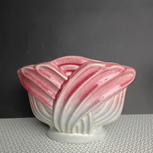 May include: A ceramic bowl featuring a sculptural, fan-like design with raised, curved ridges. The piece has a glossy finish, transitioning from a deep, vibrant pink at the top edges to a soft, creamy white at the base, creating a gradient effect.