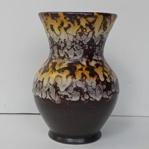 May include: A ceramic vase with a dark brown base, transitioning to a speckled pattern of white, gold, and brown. The vase has a flared top and a rounded body, suitable for floral arrangements or decorative display.