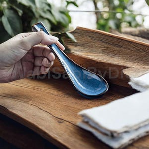 Puede incluir: Una cuchara de sopa de cerámica azul con un mango marrón oscuro. La cuchara está apoyada sobre una superficie de madera.