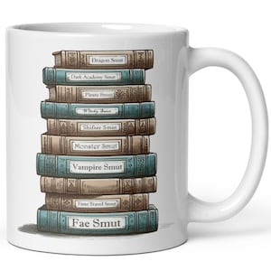 May include: White ceramic mug featuring a stack of fantasy books with titles like "Dragon Smut," "Vampire Smut," and "Fae Smut." The books are in various colors, with gold lettering. The mug has a white handle and is set against a white background.