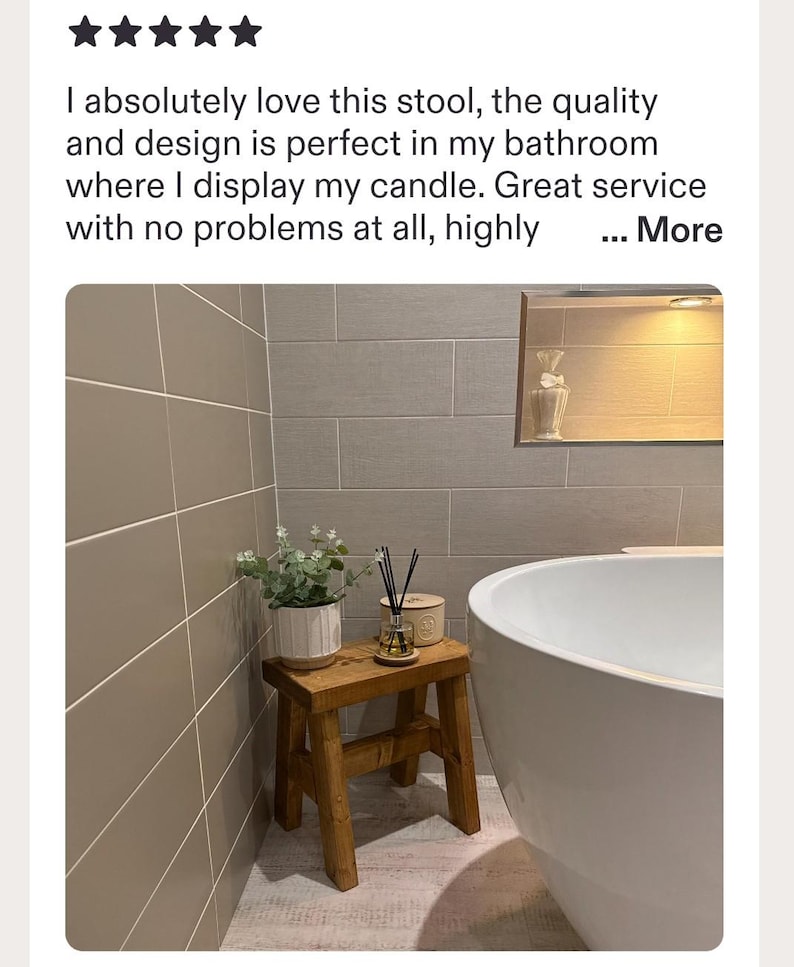 May include: A small rectangular wooden stool with four legs, supporting a white ribbed planter with green foliage and a glass reed diffuser with black sticks. The stool is positioned next to a white bathtub against a tiled bathroom wall.