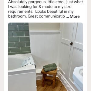 May include: A small, rectangular wooden stool with a dark brown finish and four straight legs. A folded, sage green textured towel rests on the flat top surface of the stool. The stool is positioned on a light brown wood floor in a bathroom setting.