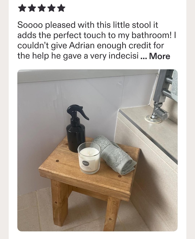 May include: A small, rectangular wooden stool with a natural finish, featuring a black plastic spray bottle, a clear glass candle with a white label, and a folded grey towel placed on its flat top surface in a bathroom setting.