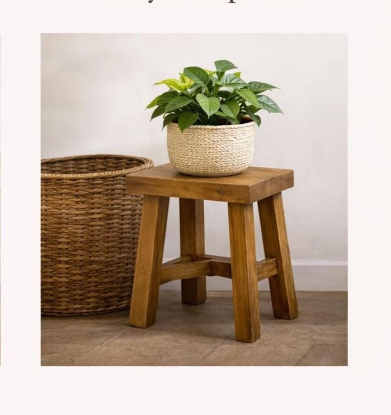 May include: A small, four-legged wooden stool with a natural brown finish, supporting a white woven basket planter containing a lush green leafy plant, positioned next to a large, tall, brown woven wicker basket with a cylindrical shape.