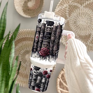 May include: A clear tumbler with a white handle and straw, featuring a design of stacked books, roses, and the text "I Prefer the Villain." The design is in shades of black, gray, and red.