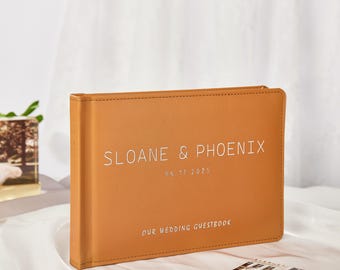 May include: A tan leather wedding guest book with the text "SLOANE & PHOENIX 06.11.2025 OUR WEDDING GUESTBOOK" in white lettering.