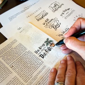 Puede incluir: Una persona est&aacute; coloreando una p&aacute;gina de la Biblia con un marcador negro, agregando color a una peque&ntilde;a ilustraci&oacute;n de una planta en maceta junto a las palabras "The Way, The Truth, The Life". Otras p&aacute;ginas presentan frases inspiradoras escritas a mano.
