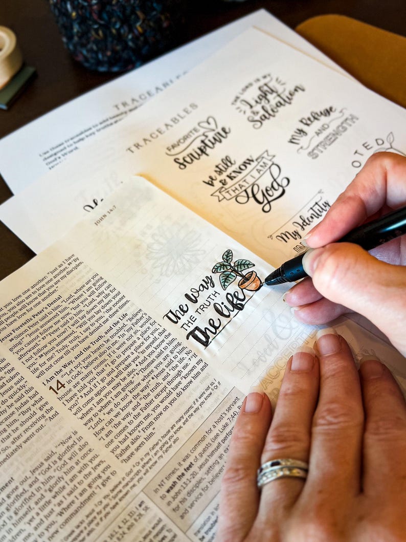 Puede incluir: Una persona est&aacute; coloreando una p&aacute;gina de la Biblia con un marcador negro, agregando color a una peque&ntilde;a ilustraci&oacute;n de una planta en maceta junto a las palabras "The Way, The Truth, The Life". Otras p&aacute;ginas presentan frases inspiradoras escritas a mano.