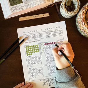 May include: A planner titled "Planted in Petition" with a calendar layout, a pen, and colored circles. The text "have faith" is on a pen holder. An open book and a decorative basket are also visible.