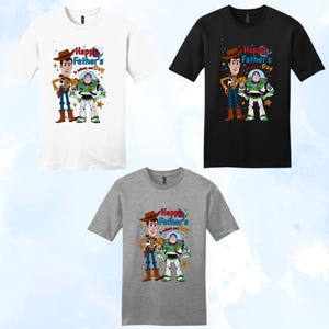 Puede incluir: Tres camisetas en blanco, negro y gris, cada una con un gr&aacute;fico de Woody y Buzz Lightyear con el texto "Happy Father's Day". Los personajes de dibujos animados est&aacute;n a color, Woody con un atuendo de vaquero y Buzz con un traje espacial.