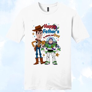 Puede incluir: Camiseta blanca con los personajes de dibujos animados Woody y Buzz Lightyear. El dise&ntilde;o incluye el texto "Happy Father's Day" y "To infinity and beyond". Woody viste un traje de vaquero, y Buzz lleva un traje espacial.