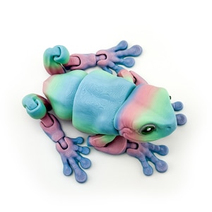 May include: A colorful, articulated lizard toy in shades of blue, pink, and green. The toy has a textured body and jointed limbs, allowing for various poses. The lizard's eyes are black, and the overall design is whimsical and playful.