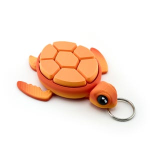 May include: Orange and red turtle keychain with a silver keyring. The turtle has a segmented shell design and detailed flippers. The turtle's head features a black eye and is made of plastic.