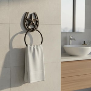 May include: Bronze-colored towel ring with a horseshoe and star design. The ring holds a folded white towel. The bathroom fixture is mounted on a light-colored tiled wall. A sink and mirror are visible in the background.