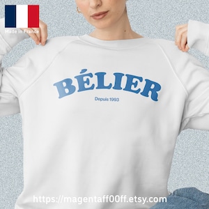 Könnte beinhalten: Weißer Pullover mit einem blauen Aufdruck, der "BÉLIER" und "Depuis 1993" lautet.