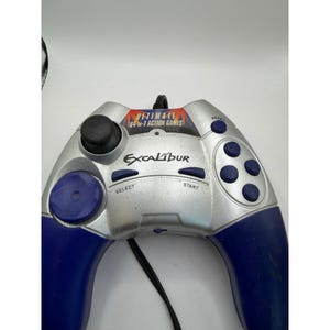 Puede incluir: Mando de juego Excalibur plateado y azul con un joystick y botones negros. El mando tiene el texto "ULTIMATE 64-IN-1 ACTION GAMES" y "Excalibur" impreso. El mando tiene un cable negro.
