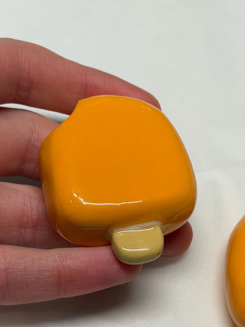 May include: A bright orange popsicle-shaped object with a light yellow stick. The object is smooth and glossy, with rounded edges. The popsicle is held in a hand.