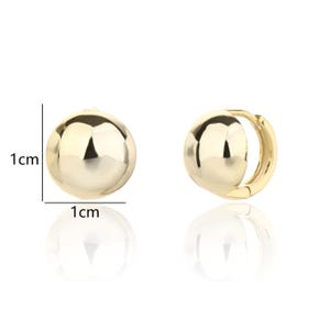 May include: A pair of gold-coloured ball-shaped hoop earrings. Each earring is approximately 1 cm in diameter. The earrings have a smooth, reflective surface and a simple, classic design. The earrings are shown against a white background.