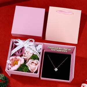 May include: A pink gift box containing a floral arrangement and a necklace with a four-leaf clover pendant. The box has a ribbon that reads "LOVE IS ETERNAL". A matching pink gift bag is also present. The text "Floral Gift Box Add-on Sold Separately" is visible.