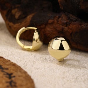Small gold ball stud earrings worn on a model, featuring a dainty yet eye-catching design. A great everyday earring choice that pairs effortlessly with any style.