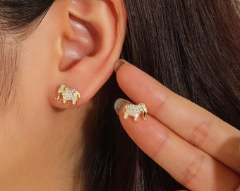 Könnte beinhalten: Ein Paar Ohrstecker in Form von goldenen Elefanten. Jeder Ohrstecker besteht aus einem polierten goldenen Umriss und einem Körper, der mit kleinen, klaren, funkelnden Steinen besetzt ist, die das Licht einfangen und eine detaillierte Optik erzeugen.