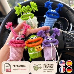 Puede incluir: Cinco pequeñas bolsas de ganchillo con forma de monstruo, coloridas, con bocas anchas, ojos móviles y mechones de hilo en la parte superior. Los monstruos son verde lima, azul, rosa, verde brillante con boca naranja y morado.