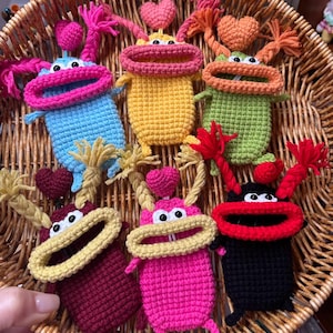 May include: A collection of colorful, handmade crochet monster keychains. Each keychain features a unique color scheme, including blue, yellow, green, pink, burgundy, and black. They have large, open mouths, heart-shaped accents, and yarn details.