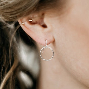 May include: A close-up of a woman's ear with a small silver hoop earring. The earring is a simple circle shape and is worn in the lower lobe of the ear.