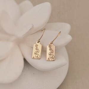 May include: A pair of gold earrings with a delicate floral design. The earrings are rectangular in shape and have a small loop at the top for hanging.