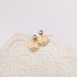 May include: A pair of gold hammered disc earrings with a small gold ball at the top of each earring.