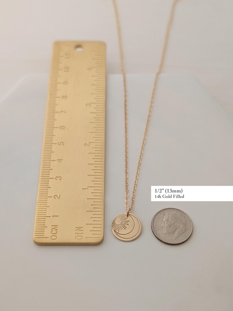May include: A gold-colored necklace with a pendant featuring a sun and moon design. The pendant is approximately 1/2 inch (13mm) in diameter. The text "14k Gold Filled" is also visible.