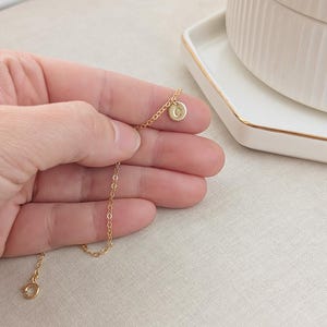 May include: A delicate gold chain necklace with a small round pendant featuring the letter "G".