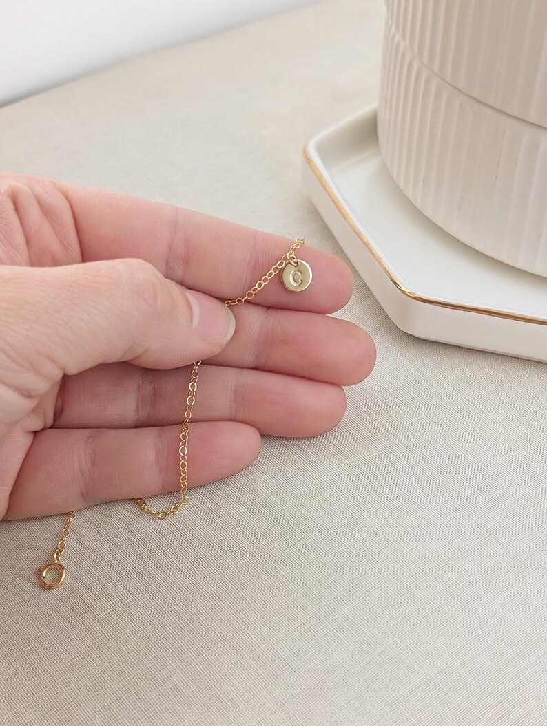 May include: A delicate gold chain necklace with a small round pendant featuring the letter "G".