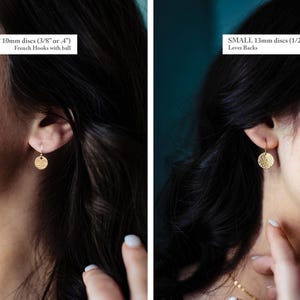May include: Gold-colored disc earrings. One earring is 3/8 inch in diameter with French hooks, and the other is 1/2 inch with lever backs. The earrings have a textured surface and are shown on a person.