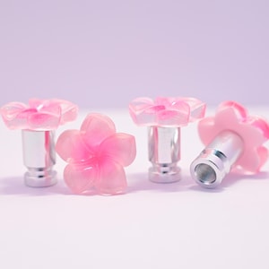 May include: Four pink flower-shaped cabinet knobs with silver metal bases. The knobs are made of translucent pink resin, with a darker pink center. One knob is lying on its side, revealing the threaded base.