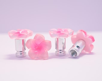 May include: Four pink flower-shaped cabinet knobs with silver metal bases. The knobs are made of translucent pink resin, with a darker pink center. One knob is lying on its side, revealing the threaded base.