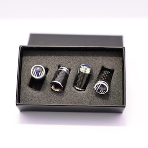 May include: Four black and silver tire valve stem caps with a thin blue line American flag design. The caps are in a black box with foam padding.