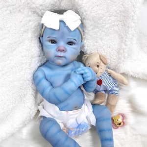 May include: A blue baby doll with white speckles and striped markings, wearing a white bow headband and a diaper. A small teddy bear in a blue and white striped shirt is next to the doll. A yellow and pink teething ring is also present.