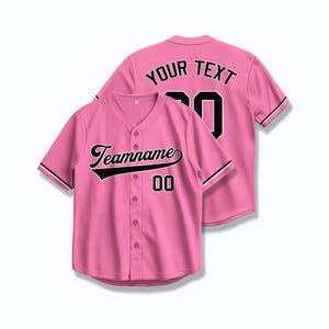 以下が含まれることがあります： ピンクのベースボールジャージに黒いトリムと黒い文字。ジャージの前面には「Teamname 00」、背面には「Your Text 00」と書いてあります。