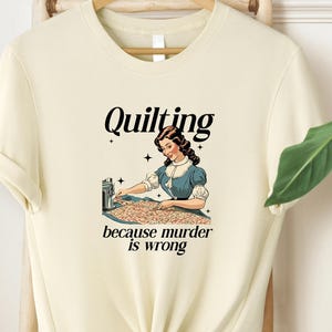 May include: A white t-shirt with a vintage-style illustration of a woman quilting. The text on the shirt reads "Quilting because murder is wrong."